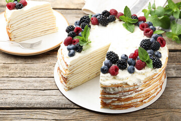Tasty crepe cake with berries and mint on wooden table