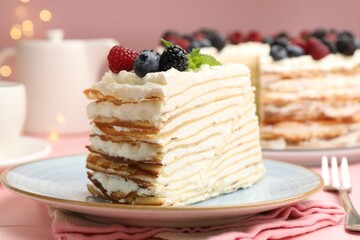 Piece of tasty crepe cake with berries served on pink wooden table against blurred lights, closeup