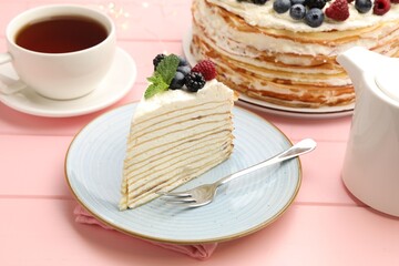 Piece of tasty crepe cake with berries served on pink wooden table, closeup