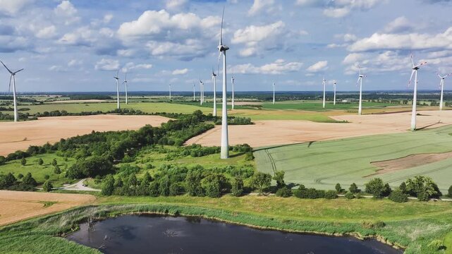 Aerial view of wind turbines standing tall in fields with a serene pond reflecting the sky, creating a harmonious blend of nature and technology, Br&uuml;ssow Uckermark, Brandenburg, Germany.