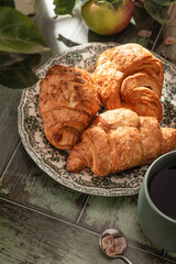 Breakfast on a wooden table with croissants, coffee and apples in bright light of the morning sun. Cozy rustic autumn food concept