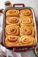 Freshly baked cinnabon buns in a ceramic baking dish on light gray background. Making cinnamon rolls process