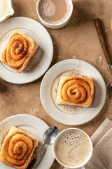 Freshly baked cinnabon roll buns served on ceramic plates with coffee on brown textured background. Cozy autumn breakfast concept. Top view