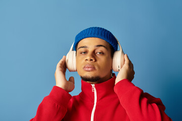 Stylish young man enjoys music against a vibrant blue backdrop with a trendy beanie