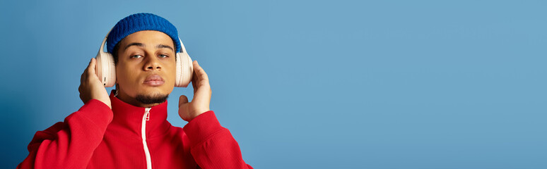 Young man in a beanie and headphones enjoys music against a blue backdrop