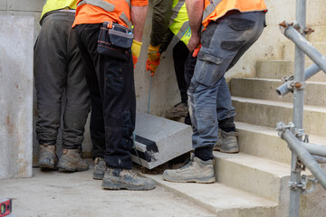 Team of builder workers lifting heavy concrete block for stairs construction. Teamwork and determination as a path to success concept.