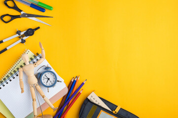 School supplies on a bright yellow background: colored pencils, notebooks, alarm clock, pencil case. Education concept, preparation for school