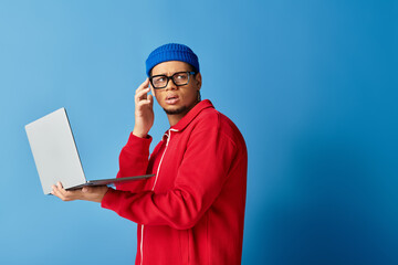 Stylish young african american man in beanie displays tech savvy on blue backdrop