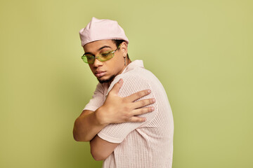 Stylish young Black man in trendy pink outfits poses against a green background