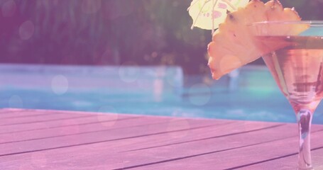 Displaying martini glass with pineapple slice and umbrella sitting on wooden pool deck, copy space