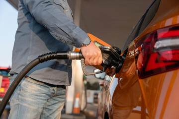Close-up of a Man refuelling orange car at gas fuel station. Male filling diesel at petrol station...