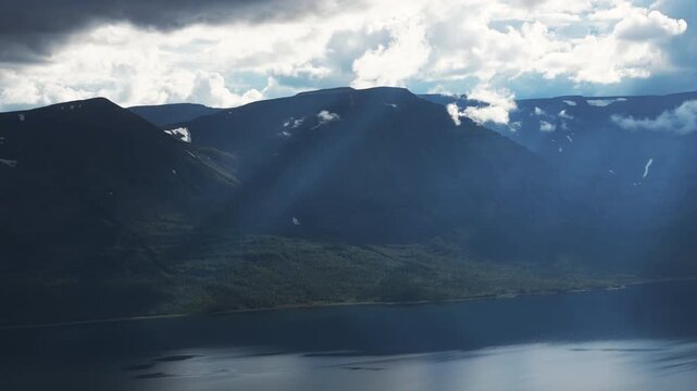 Aerial view captures a sunbeam piercing storm cloud over the Putorana Plateau ridge and reflecting on Lake Lama. Evening atmosphere and rugged mountain profile meet calm water and long shoreline