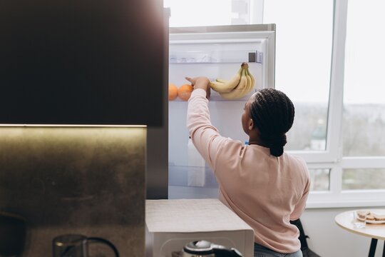 Woman reaching for oranges and bananas in refrigerator at home