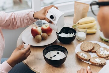 Two black women pouring milk into oatmeal at breakfast table