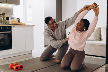 Personal trainer helping young woman stretching at home
