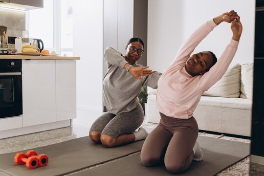 Personal trainer guiding client stretching at home - Powered by Adobe