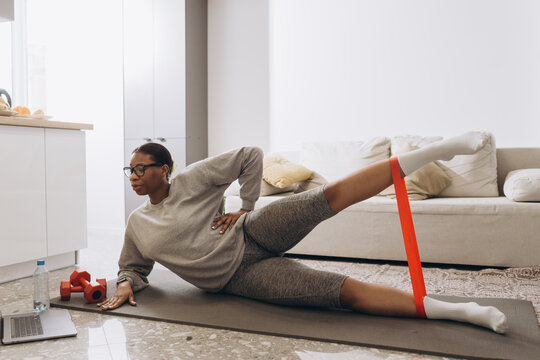 Woman doing home workout using resistance band and watching online tutorials on laptop - Powered by Adobe