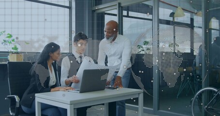 Leaning colleagues in business attire reviewing documents on laptop at office desk with world map