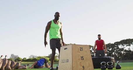 Working out man in green tank top beside plyometric box on park grass, with fitness equipment