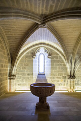 medieval baptismal font in a cathedral with a window backlit in the background