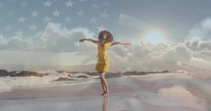 Dancing barefoot woman in yellow dress twirling on wet sand beach, with faint American flag overlay