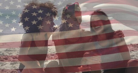 Leaning three women friends in swimsuits holding smartphone on beach, with American flag overlay