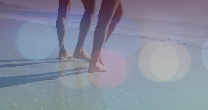 Walking couple in swimwear along wet sandy shoreline, with gentle surf foam and light bokeh