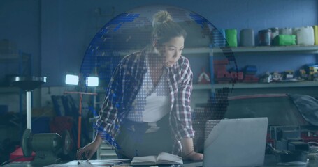 Leaning Asian woman mechanic wearing plaid shirt, jeans, checking laptop in garage, with car engine