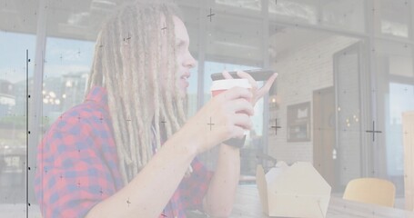 Male with dreadlocks wearing plaid shirt speaking into smartphone at cafe, with cup, takeout box