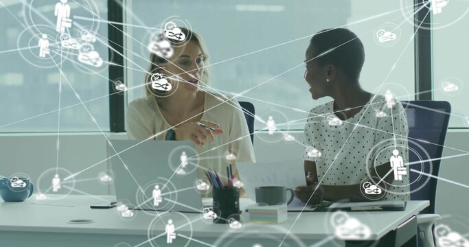 Collaborating colleagues in polka dot, cream tops at office desk, with laptop network icons
