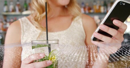 Woman holding smartphone and cocktail glass in glittery top at bar, with ice, straw, lime, mint