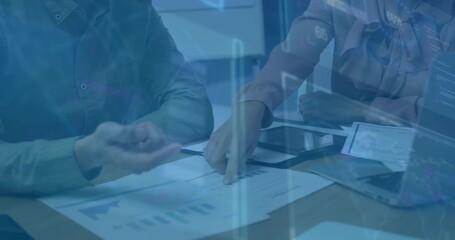 Coworkers in business attire reviewing overlaid charts at conference table with laptop, smartphone