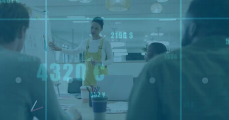 Presenting woman in yellow overalls pointing at flip chart in office, with laptops and data overlay