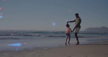 Spinning father in green shirt and son dancing at sandy beach, footprints visible, copy space