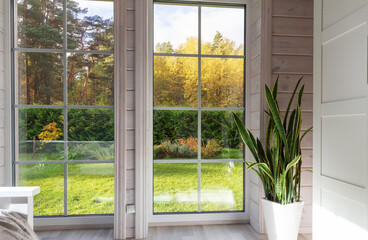 Modern interior with large panoramic windows, autumn forest view, cozy home with green plant Sansevieria in white pot, minimalistic design, natural light, seasonal lifestyle background, copy space