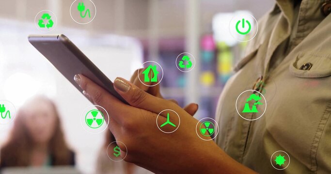 Businesswoman wearing blazer tapping tablet in office, with floating sustainable energy icons