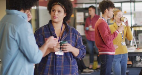 Adult woman wearing plaid shirt holding coffee mug listening to coworker in break area, copy space