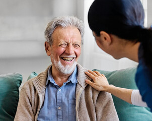 Doctor or nurse caregiver with senior man talking and having fun at home or nursing home