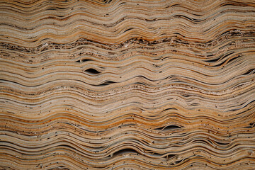 Close-up of stacked veneer wood sheets with natural wavy textures and organic lines, showing intricate patterns and fine grain in a woodworking setting.