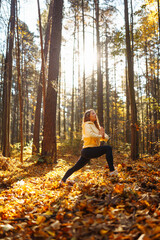 Relaxed woman practicing yoga poses, spreading arms in sunny autumn forest. Young woman enjoying...