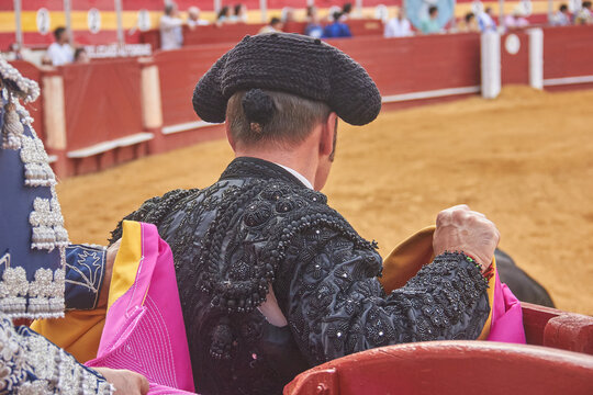 A close shot of a matador in an embroidered black suit and montera holding a pink and yellow cape during a bullfight in Almeria, Spain. Culture, heritage