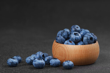 Fresh ripe blueberries in small wooden bowl on dark gray textured stone background. Delicious organic fruit rich in vitamins, wild berries,healthy lifestyle, natural food. Close up, macro