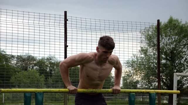 Male shirtless athlete doing push ups on parallel bars at nature. Strong sporty man exercising at sports ground. Young sportsman training hard outdoor. Concept of active sportive lifestyle. Slow mo