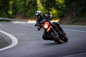 Naklejka premium Motorcyclist Riding Orange Motorcycle on Curved Road Outdoors