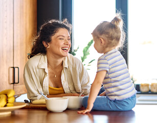 Portrait of a mother and daughter preparing and eating breakfast and having fun in the kitchen at home