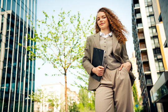 Confident young businesswoman outdoors, dressed formally while holding documents and exuding professionalism