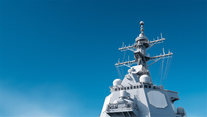 Fototapeta premium Modern warship with antennas and radar tower under clear blue sky, symbolizing defense, navy and maritime security. Bright sky background offers ample copy space for concepts and advertising.