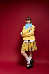 Young woman in cheerful yellow outfit embraces study materials against vibrant red backdrop