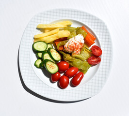white plate with cucumber slices, potato chips, cherry tomatoes, baked peppers and yogurt sauce isolated on white background top view 