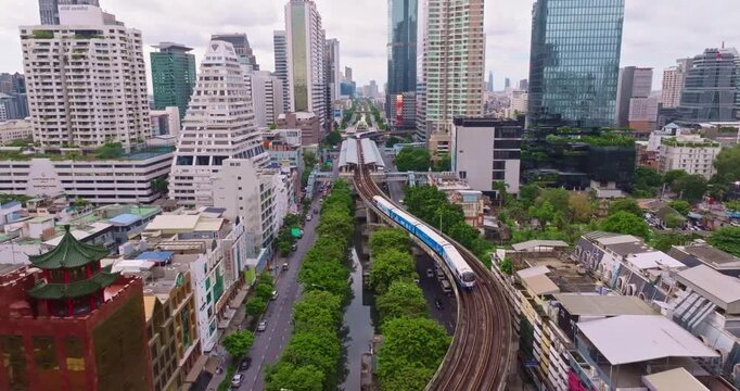 Aerial View of Bangkok City Showcasing Skyscrapers and Train on Elevated Tracks Amidst Urban Greenery and Bustling Landscape